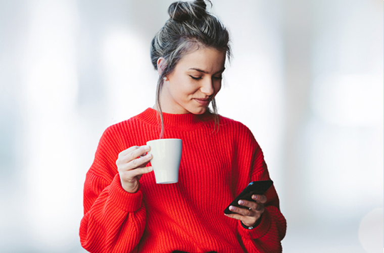 Photo of a woman looking at her mobile phone while drinking a coffee